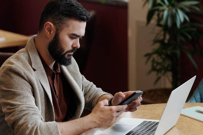 schedule c tax form man texting on phone while sitting in front of laptop in a cafe