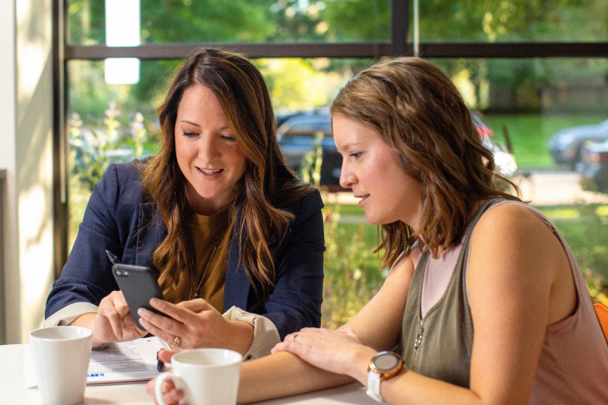 2 women in office, drinking coffee and looking at mobile phone